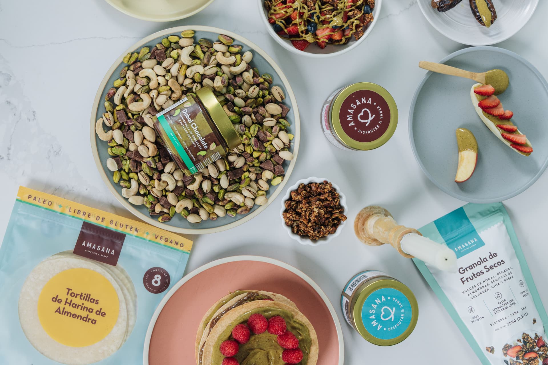 Mesa con productos AMASANA: tortillas de harina de almendra, granola de frutos secos, mantequillas, frutos secos y panqueques